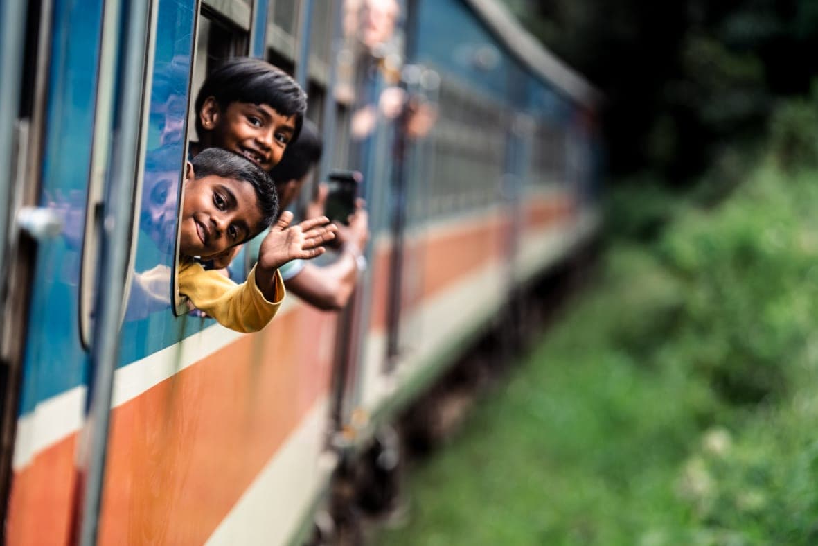 Two children leaning out of a moving train window, laughing and waving
