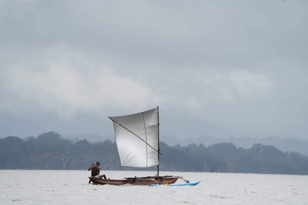 A lone fisherman steering a traditional sailboat across a misty lake