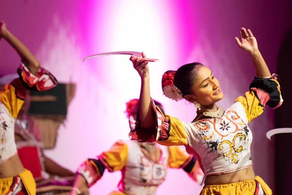 A Kandyan dancer mid-spin in a bright batik costume under stage lights