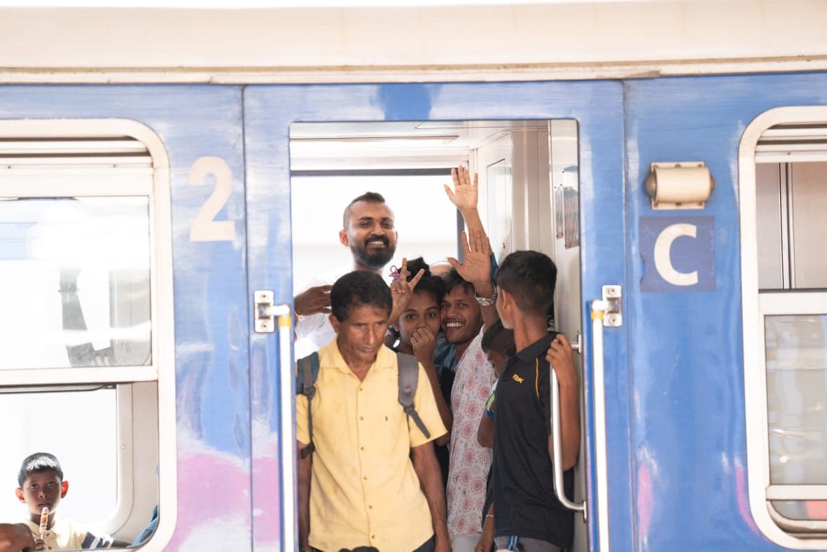 Passengers crowding a train doorway, waving and flashing peace signs