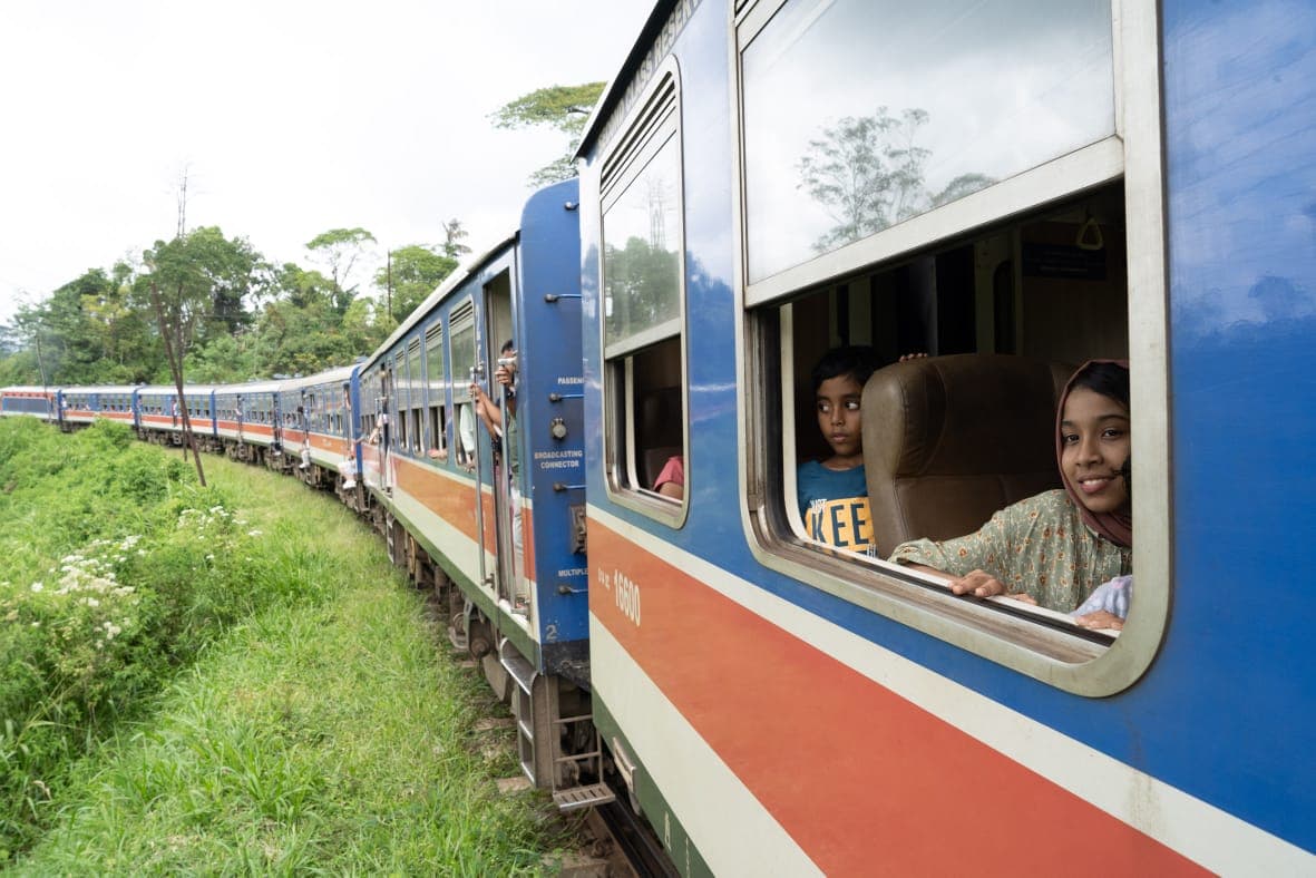 A girl and a boy watching the hill country roll past from a train carriage